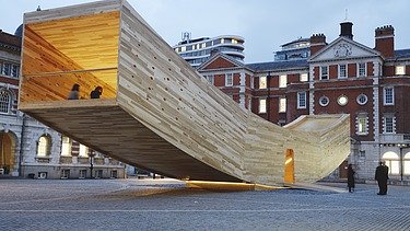 Photo of the curved wooden sculpture The Smile in London. The wooden box can be walked on and is intended to represent a smiling mouth.