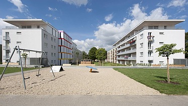 Photo of two multi-storey buildings with garden in front. Wooden extensions.