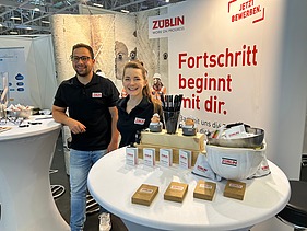 Fotos eines Messestandes von ZÜBLIN Timber. Zwei Personen sind zu sehen.