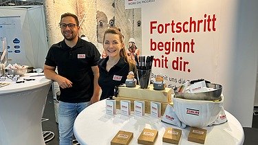 Fotos eines Messestandes von ZÜBLIN Timber. Zwei Personen sind zu sehen.