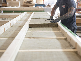 Photo of a LENO ADD element. A commercial employee of ZÜBLIN Timber is placing the wood fiber boards into the element.