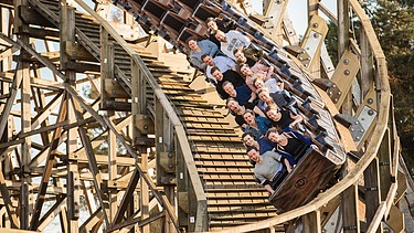 Photo of a roller coaster with wooden rails and people inside.