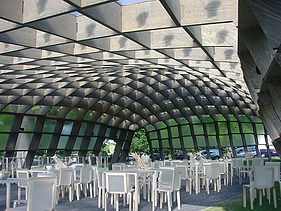 Foto des bestuhlten Innenraumes des Serpentine Pavillons in London. Man sieht eine schöne Holzkonstruktion des Daches.
