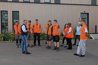 Group photo of the new trainees wearing high-visibility vests during a company tour.