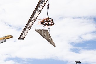 Photo of a wooden gable wall element suspended from a crane above the Schule am Hangs in Frankfurt.
