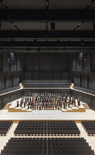 Interimsspielstätte Gasteig München Foto der Interimsspielstätte Gasteig in München. Zu sehen ist der bestuhlte Bühnenraum mit Orchester.