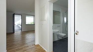 Foto einer leeren Wohnung. Zu erkennen ist ein Wohnraum und Badezimmer.
