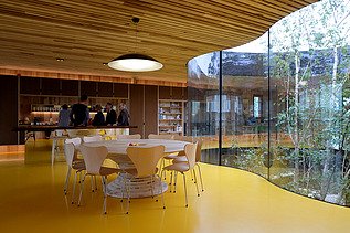 Photo of an interior with large glass window front, wooden ceiling and table with chairs.