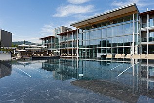 Photo of the Hotel Aqualux ini Bardolino. You can see a large building with a glass façade and flat roof, as well as a pool.