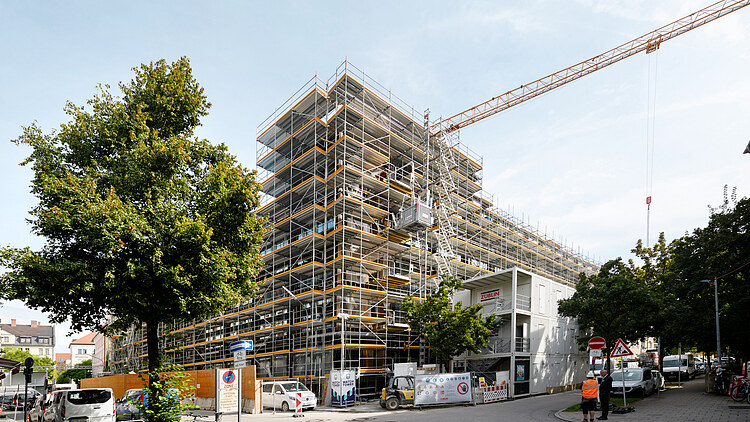 Fotos des Rohbaus VINZENT in München. Man sieht ein mehrgeschossiges, eingerüstetes Gebäude.