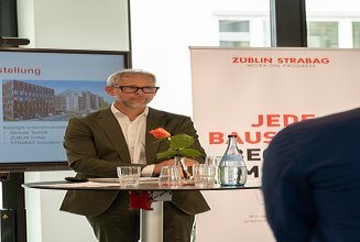Foto von drei Personen in einem Innenraum. Im Hintergrund ist ein Monitor und Roll-Up zu sehen.