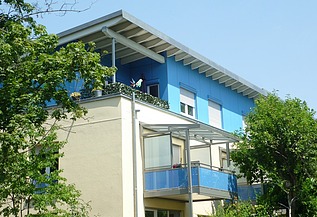 Aufstockung Gartenstadt Karlsruhe Foto eines mehrgeschossigen Gebäudes mit weiß-blauer Fassade.