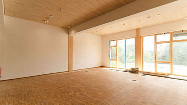 Foto der Uni Witten von innen. Man sieht einen Innenraum mit vielen Holzoberflächen.