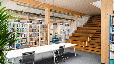 Photo of the library at Witten University. You can see lots of books, a wooden ceiling and wooden stairs.