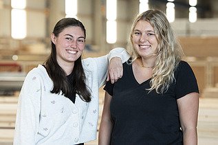 Foto von zwei jungen Frauen, die in die Kamera lächeln.