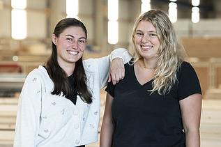 Foto von zwei jungen Frauen, die in die Kamera lächeln.