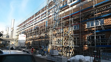 Foto eines eingerüsteten, mehrgeschossigen Gebäudes. Man sieht eine Aufstockung aus Holz.