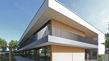 Außenaufnahme der Kita in Frankfurt. Man sieht ein Gebäude aus Holz mit Flachdach.