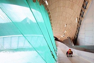Photo of a bobsleigh run with a wooden roof and a lying bobsleigh rider in red clothing