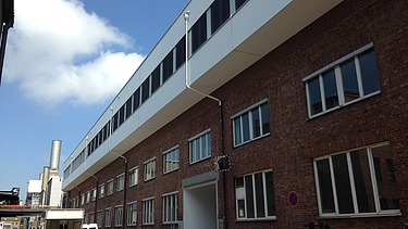 Photo of a multi-storey building. Wooden extension with white façade and flat roof.