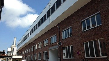 Photo of a multi-storey building. Wooden extension with white façade and flat roof.