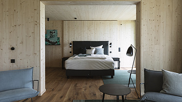 Foto eines Wohnraumes von Innen. Bett, Stühle und Holzwände.