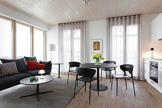 Foto eines möblierten Wohnraumes, des Holzgebäudes CARL in Pforzheim. Couch und Tisch mit Stühle.