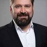 Photo of a smiling man with a full beard, black jacket and white shirt. Thees Hargus.