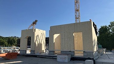 Baustellenfoto, auf dem die Montage der ersten Brettsperrholzelemente zu sehen ist.