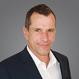 Kontakt ZÜBLIN Timber: Christof Mayr Foto eines lachenden Mannes, schwarzem Jackett und weißem Hemd. Christof Mayr.