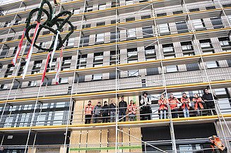 Foto vom Richtfest des Büroneubaus T3 in Aichach. Der Richtkranz wird hochgezogen. Es stehen Personen auf dem Gerüst.