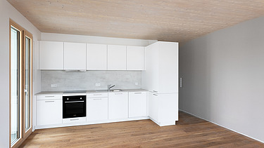 Foto eines möblierten Wohnraumes, des Holzgebäudes CARL in Pforzheim. Man sieht eine weiße Küche.