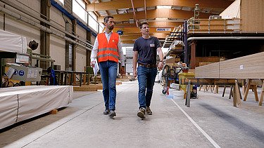 Foto von zwei Männern, die in einer Produktionshalle von Holzelementen laufen