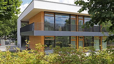Exterior shot of the daycare center in Frankfurt. You can see a wooden building with a flat roof.