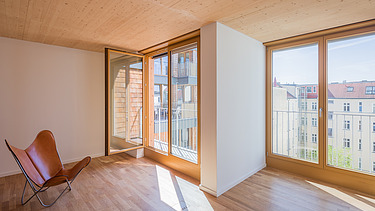 Photo of an interior with a wooden ceiling and large windows and a red chair inside.