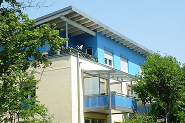 Foto eines mehrgeschossigen Gebäudes mit weiß-blauer Fassade.