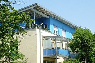 Aufstockung Gartenstadt Karlsruhe Foto eines mehrgeschossigen Gebäudes mit weiß-blauer Fassade.
