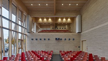 Foto eines Raumes mit roter Bestuhlung und vielen Holzoberflächen. JOWAT Haus der Technik.