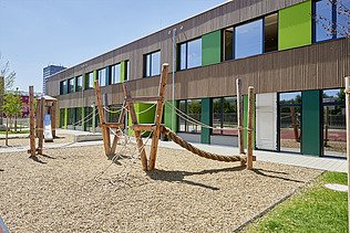 Photo of a wooden school from the outside. You can see the wooden building and the garden area.