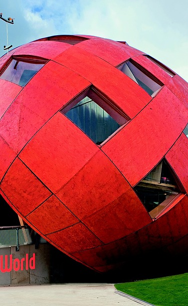 Regierungspavillion Floriade NL-VENLO Foto eines rießigen, schrägliegenden Holzeis mit orangefarbiger Holzfassade und Fenstern.