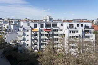 Foto eines mehrgeschossigen Gebäudes mit weißer Fassade. Aufstockung aus Holz.