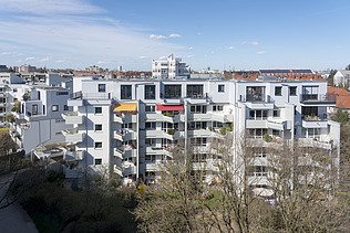 Foto eines mehrgeschossigen Gebäudes mit weißer Fassade. Aufstockung aus Holz.