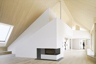 Photo of a modern interior with a striking wood-burning stove in the middle of the room and visible sloping LENO wall elements.