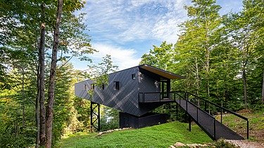 Photo of a wooden house on steel stilts in the middle of the forest.