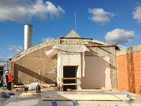 Foto einer Baustelle. Man sieht den alten Steinkern des Gebäudes auf dem mit Holz aufgestockt wird.