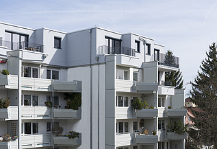 Aufstockung Klingerstraße München Foto eines mehrgeschossigen Gebäudes mit weißer Fassade. Aufstockung aus Holz.
