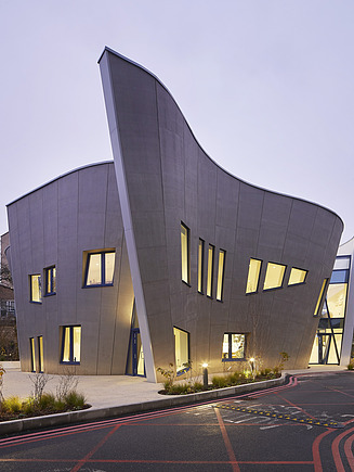 Außenansicht des Maggie Center in London. Man sieht ein geschwungenes Gebäude aus Holz.