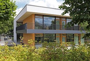 Außenaufnahme der Kita in Frankfurt. Man sieht ein Gebäude aus Holz mit Flachdach.