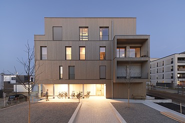 Baugemeinschaft Würzburg Nachtaufnahme eines mehrgeschossigen Gebäudes aus Holz.