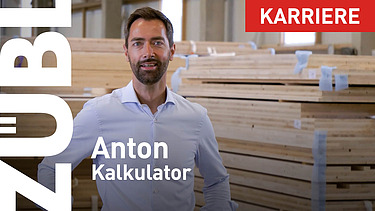 Photo of a man smiling and looking into the camera. A pile of wood can be seen in the background